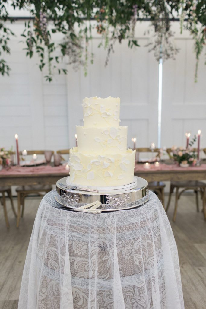 A bridgerton themed three tier wedding cake with floral behind