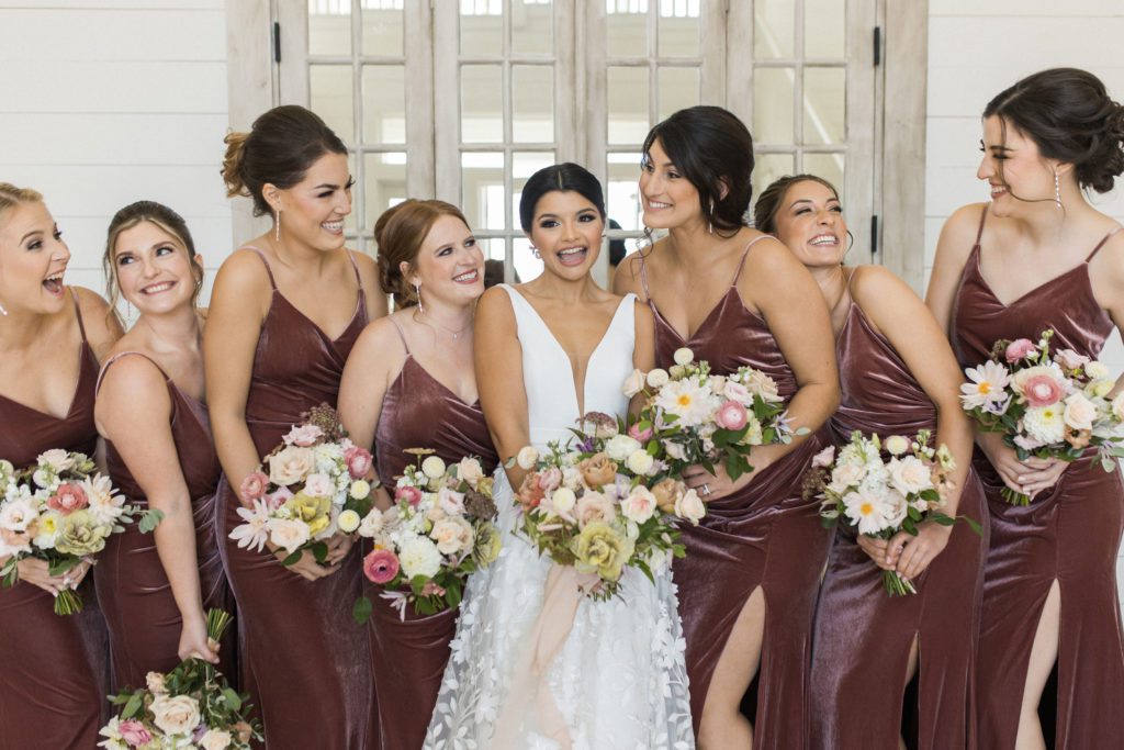 Bride and bridesmaids smiling for a photo in their blush velvet bridesmaids dresses. 